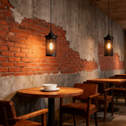 Single retro industrial pendant lights with a black wire cage casting warm light over a wooden cafe table and distressed brick wall.