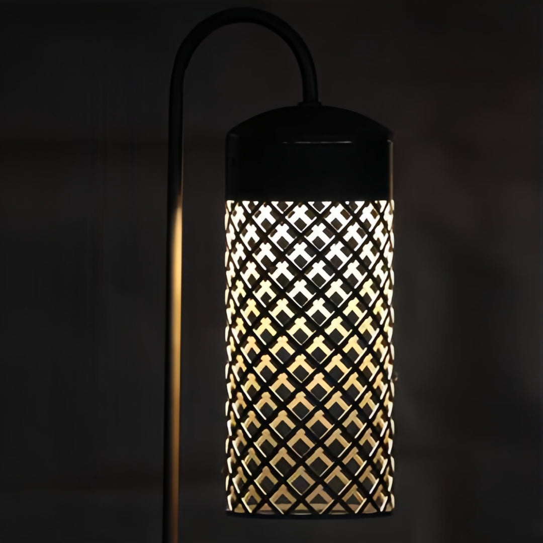 Single black outdoor pendant lantern with a curved shepherd's hook arm, illuminating a path or garden corner at night.
