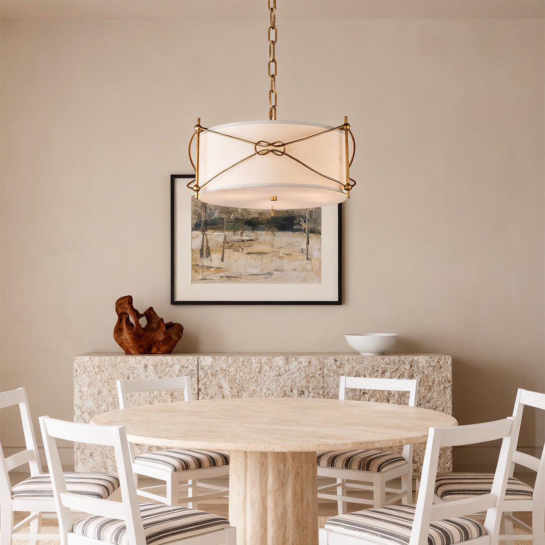 Single white drum pendant light fixture providing soft light over a round travertine dining table in a bright, modern casual space.