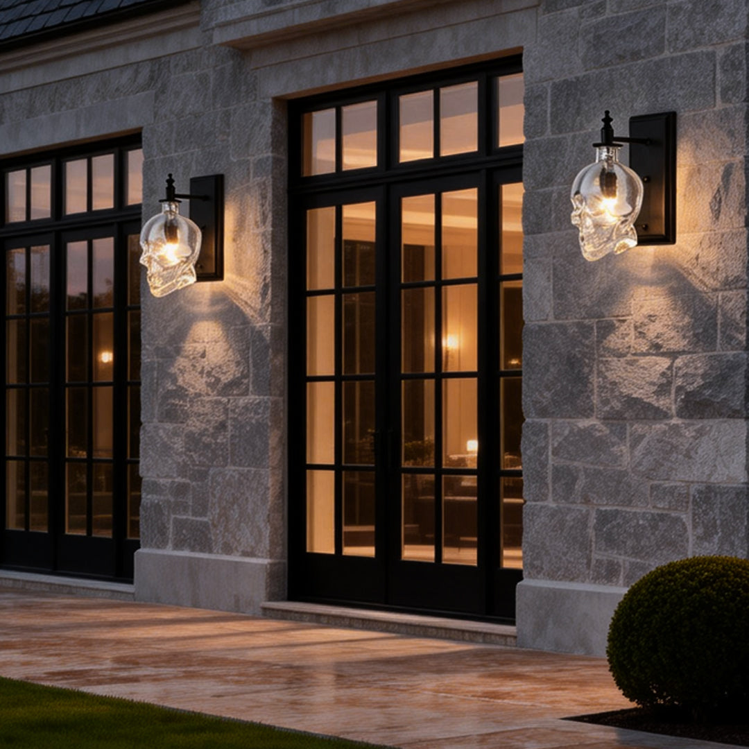 Unique glass lamp shades for wall lights in skull design, mounted outside a modern house with stone walls and large windows.