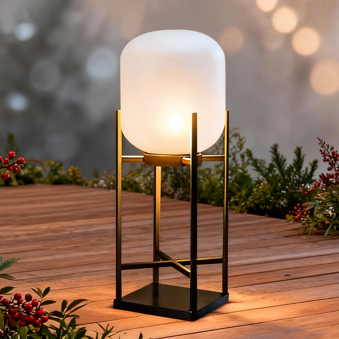 Outdoor standing light with sleek black design and frosted shade on wooden deck by the water.