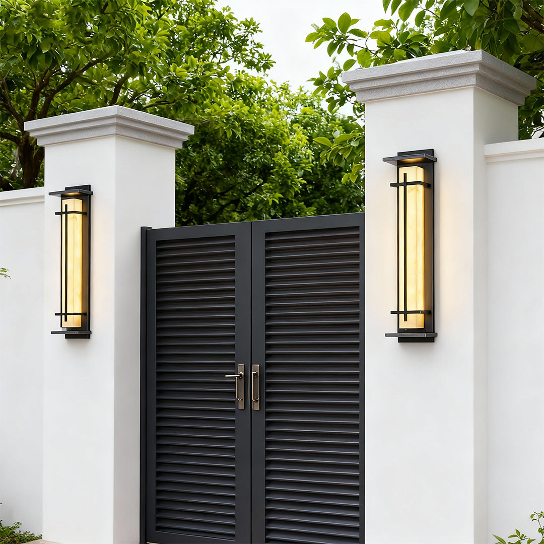Two sleek black outside wall lights mounted on white pillars flanking a modern dark gate.