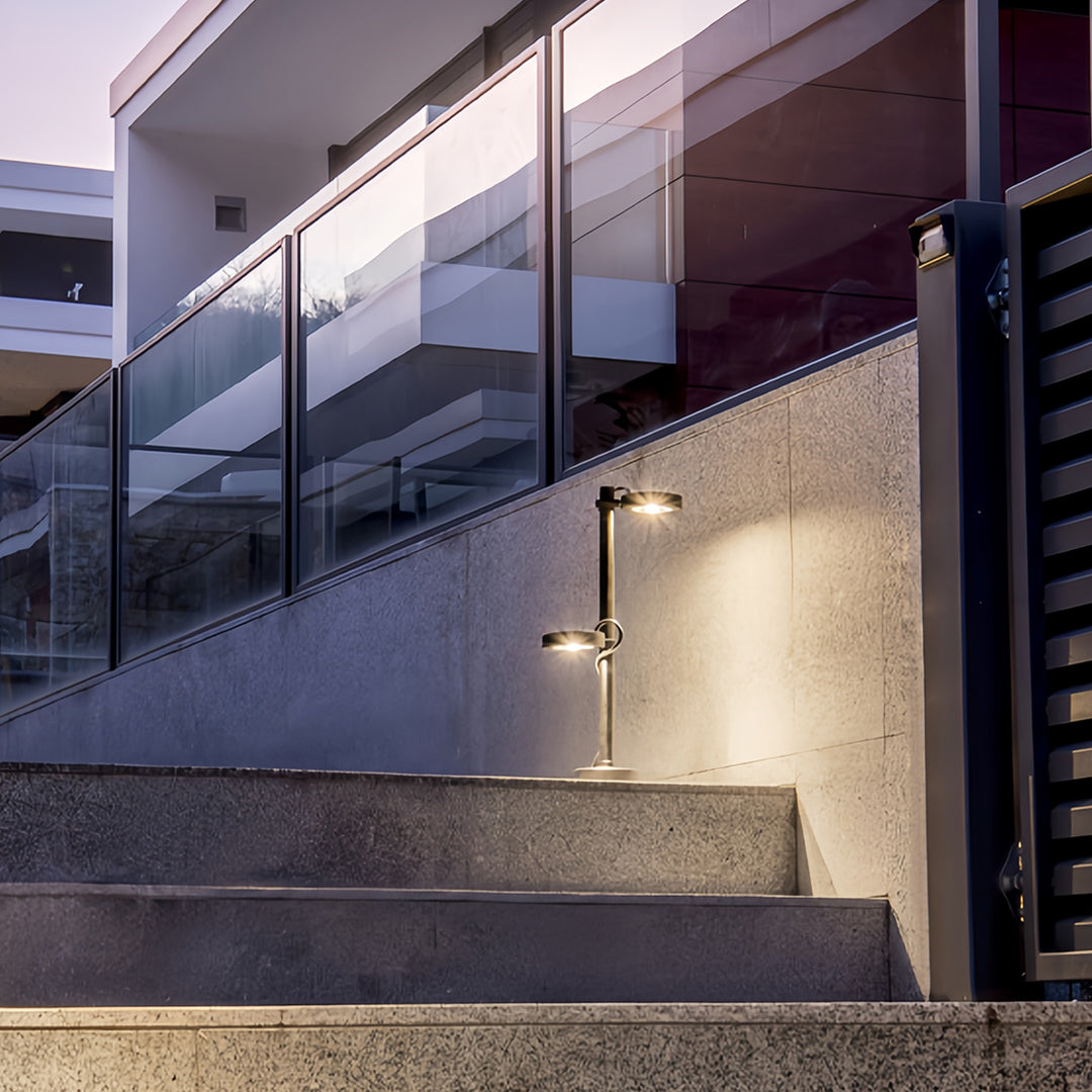 Sleek black dual-head pathway landscape lights illuminating concrete exterior stairs and a modern glass balustrade.