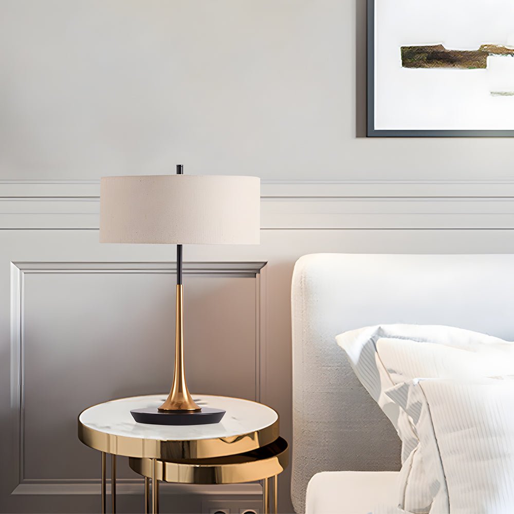 Sleek fabric table lamp with gold trumpet base on a luxury marble nightstand in a white bedroom.