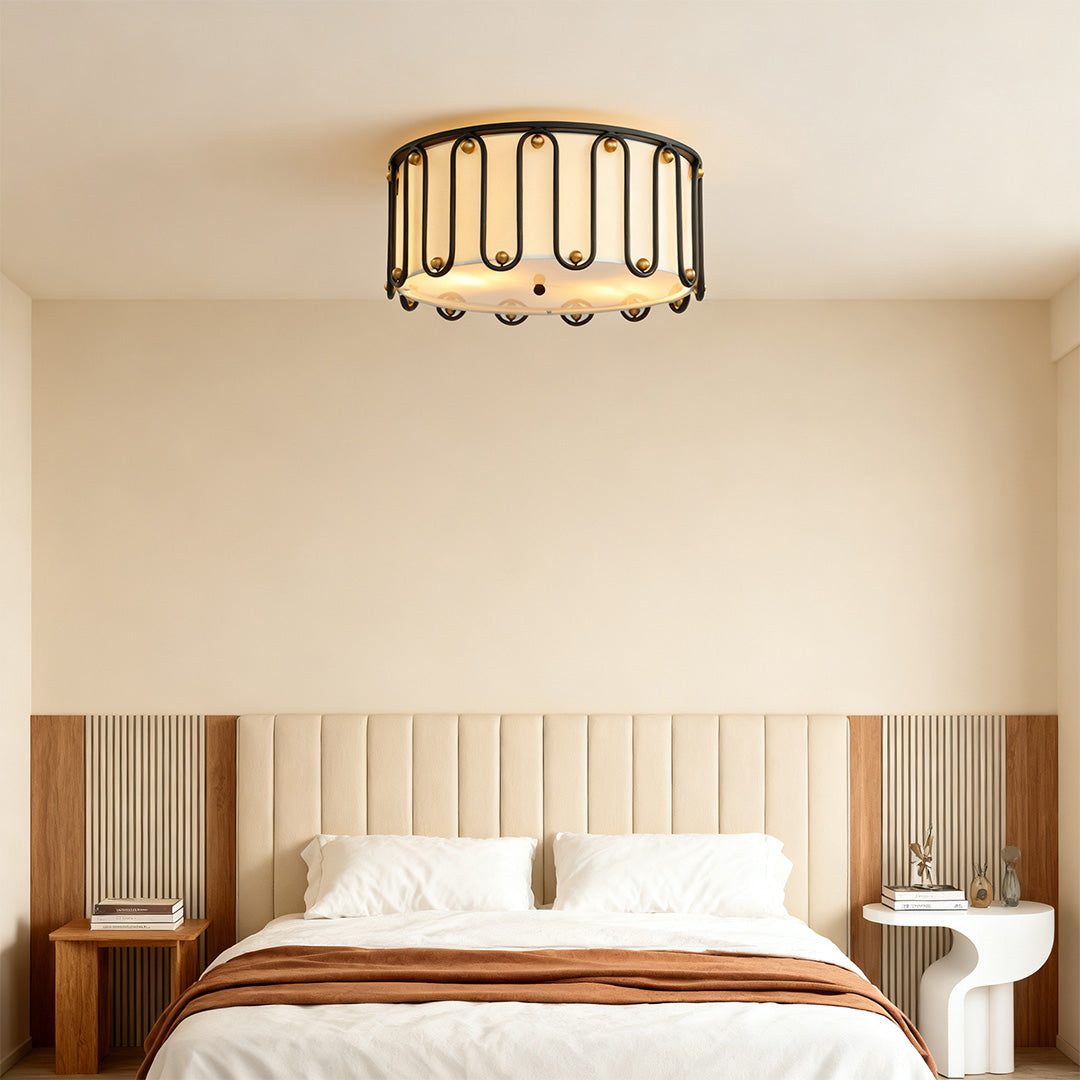 Sleek drum ceiling light flush mount fixture illuminating a modern bedroom with a cream-colored upholstered headboard and wood accents.