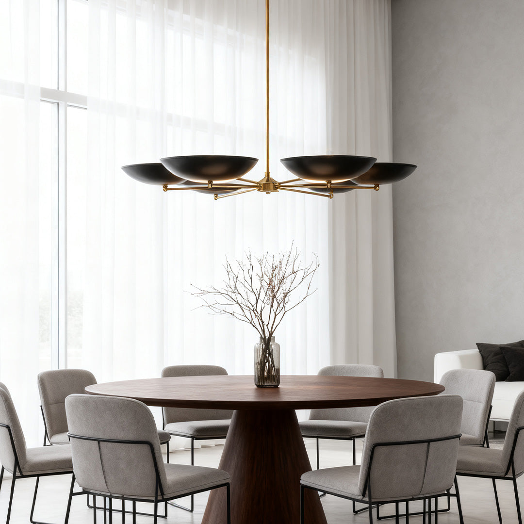 Sleek black and gold chandeliers casting light over a round wood dining table in a minimalist, light-filled contemporary dining area.