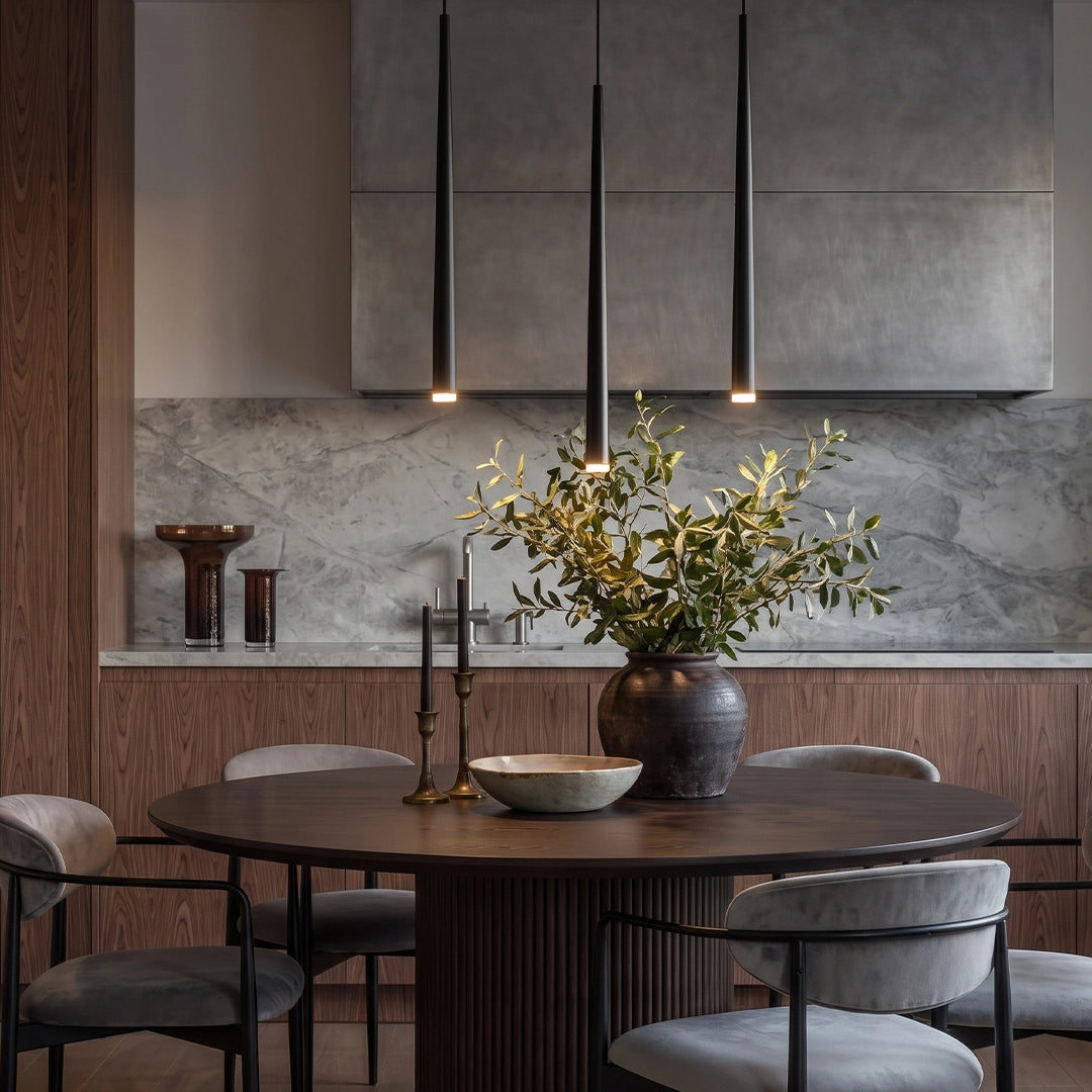 Slim black pendant light above a round dining table in a contemporary dining room with warm wood cabinetry.