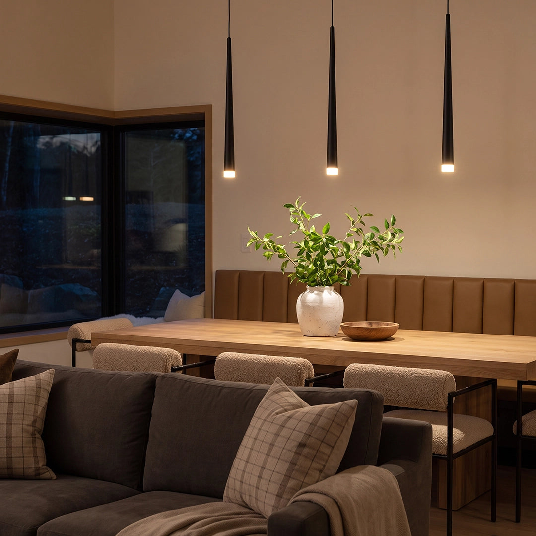 Slim black pendant light over a modern wooden dining table in an open-plan living and dining room.