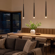Slim black pendant light over a modern wooden dining table in an open-plan living and dining room.