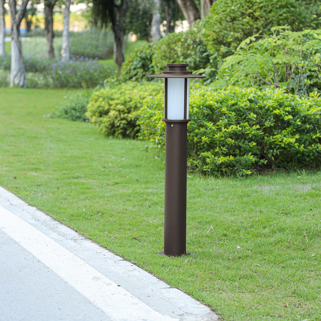 Slim cylindrical outdoor path light installed next to a road in a green lawn