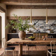 Slim gold cone pendant lights hanging above a rustic dining table in a warm kitchen with exposed wood beams.