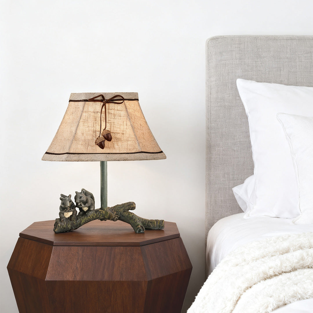 Small accent squirrel table lamp providing soft ambient light on a dark geometric nightstand in a cozy bedroom setting.