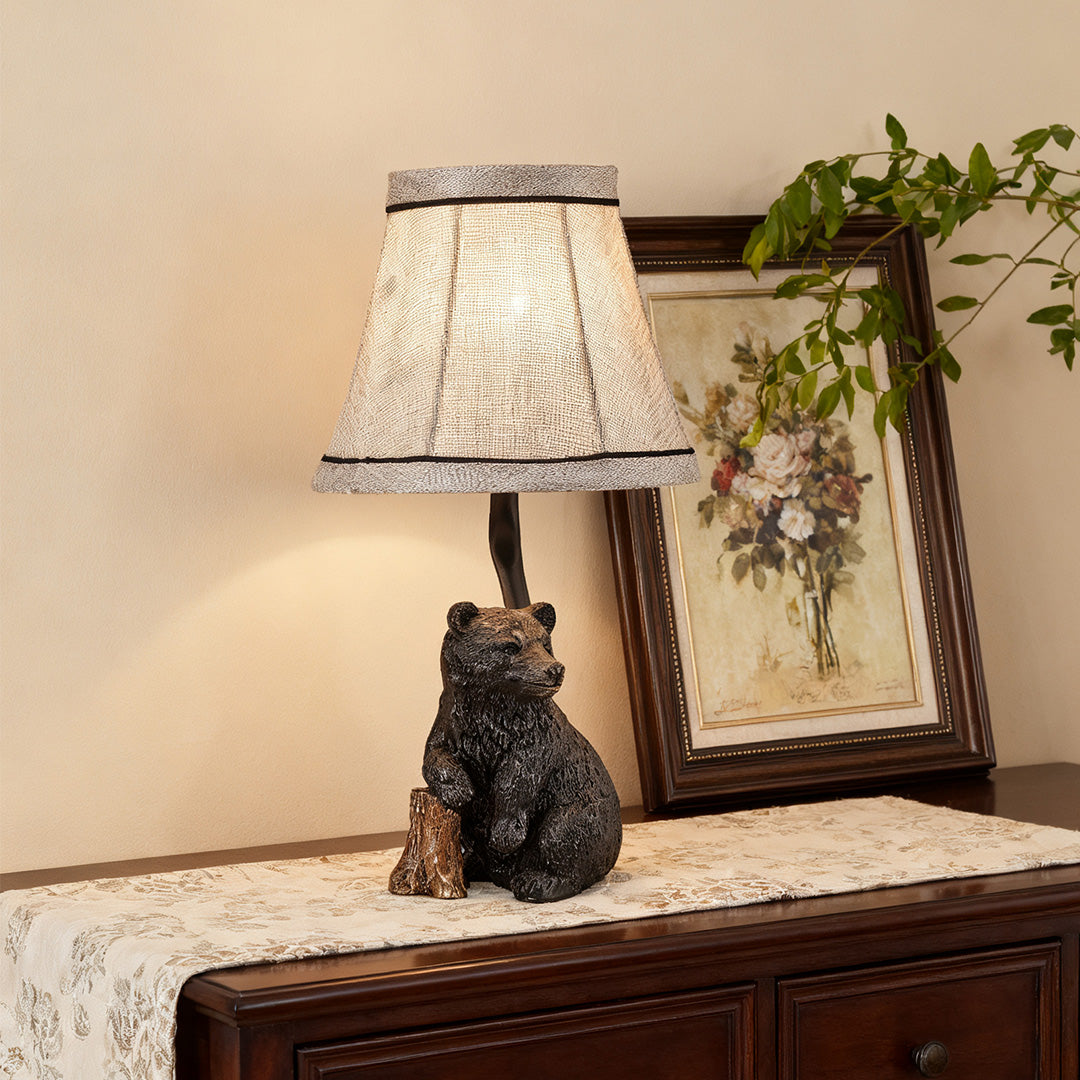 Small accent resin table lamp with a textured shade and wildlife base, sitting on a dresser or console table with framed art.