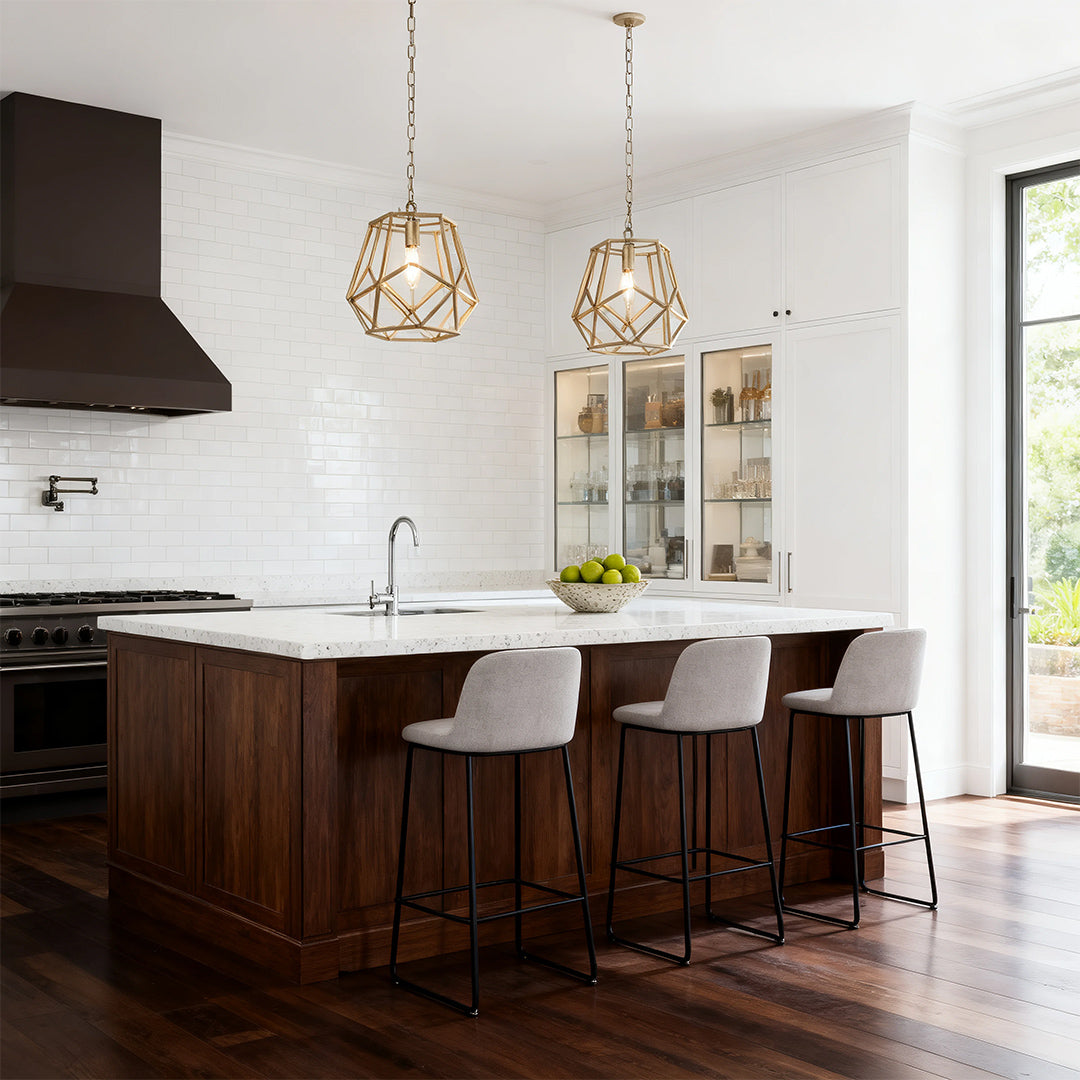 Small geometric gold hanging pendant light with an open brass cage, suspended over a dark wood kitchen island with white countertop.