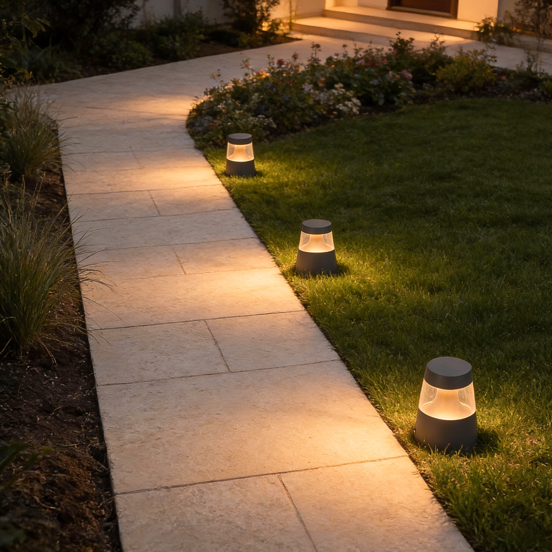 Small landscape lights evenly spaced along a curved garden path, creating subtle guidance lighting across grass and paving.