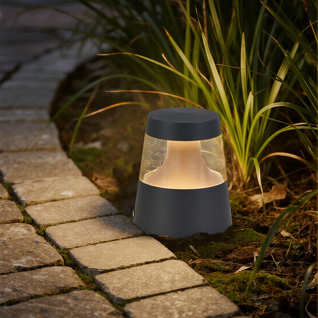 Small landscape lights placed beside stone edging and ornamental grass, providing soft pathway illumination for a residential garden setting.