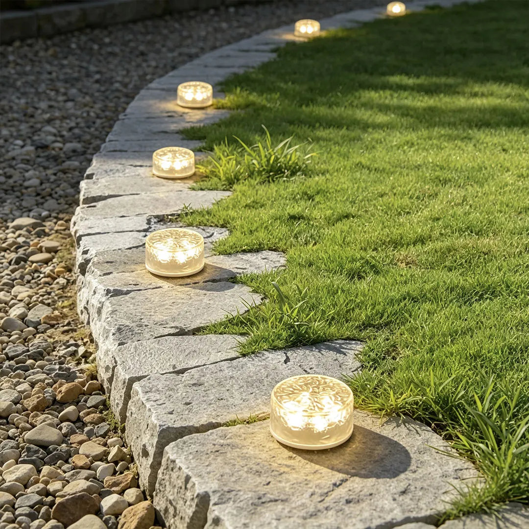 Small step lights placed along a curved stone border beside a lawn for warm pathway illumination.