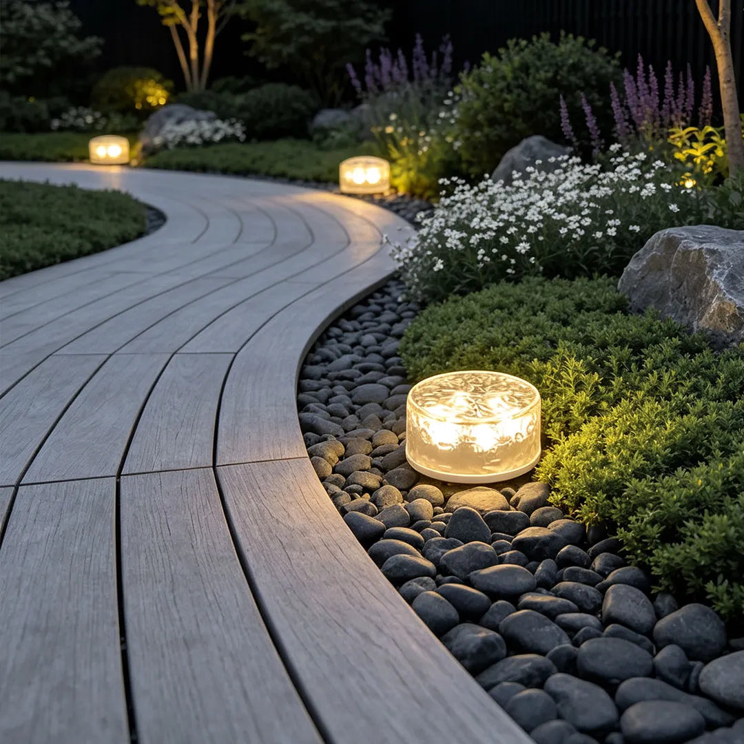 Small step lights illuminating a winding garden path with pebbles, shrubs, and soft landscape lighting.