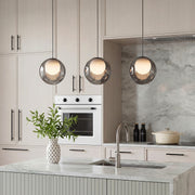 A trio of smoked glass pendant lights hanging over a modern marble kitchen island with cabinets.