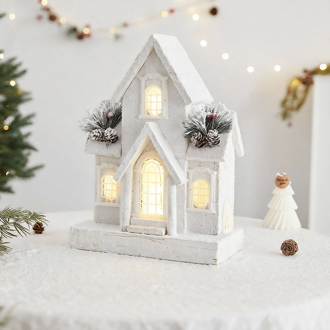 Snow-covered white church design representing light up wooden christmas houses with festive pine cones.