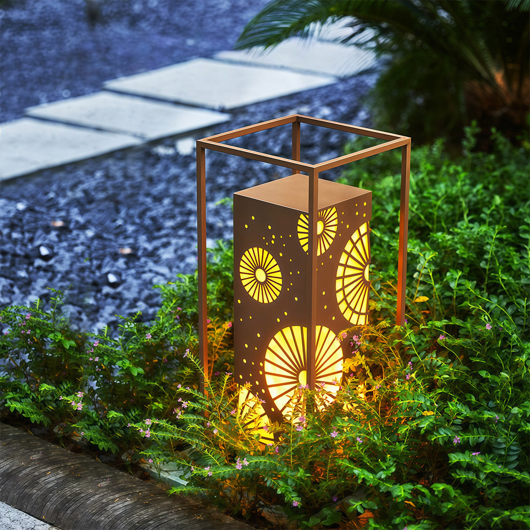 LED bollard light with a decorative pattern providing soft, warm illumination in a garden landscape.