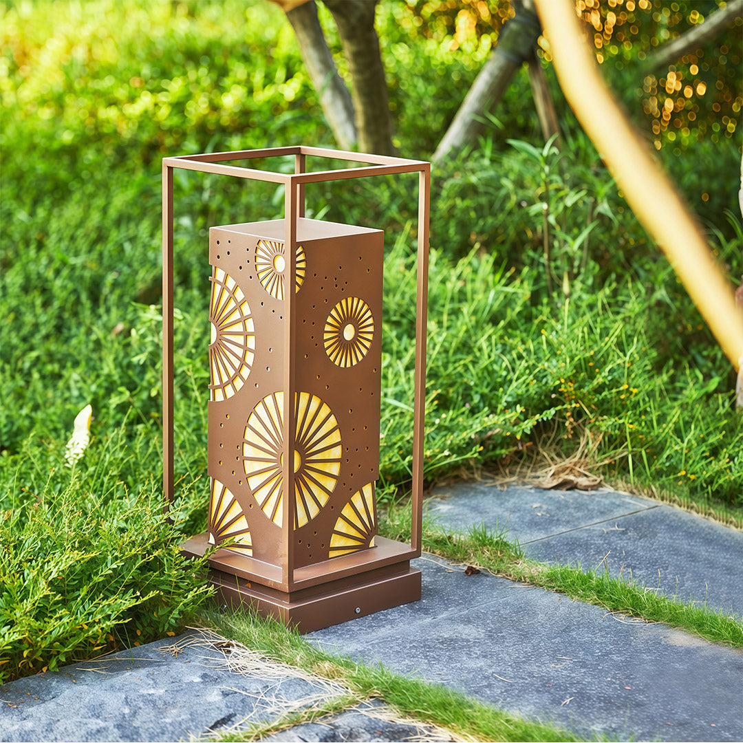LED bollard light with a decorative pattern providing soft, warm illumination in a garden landscape.