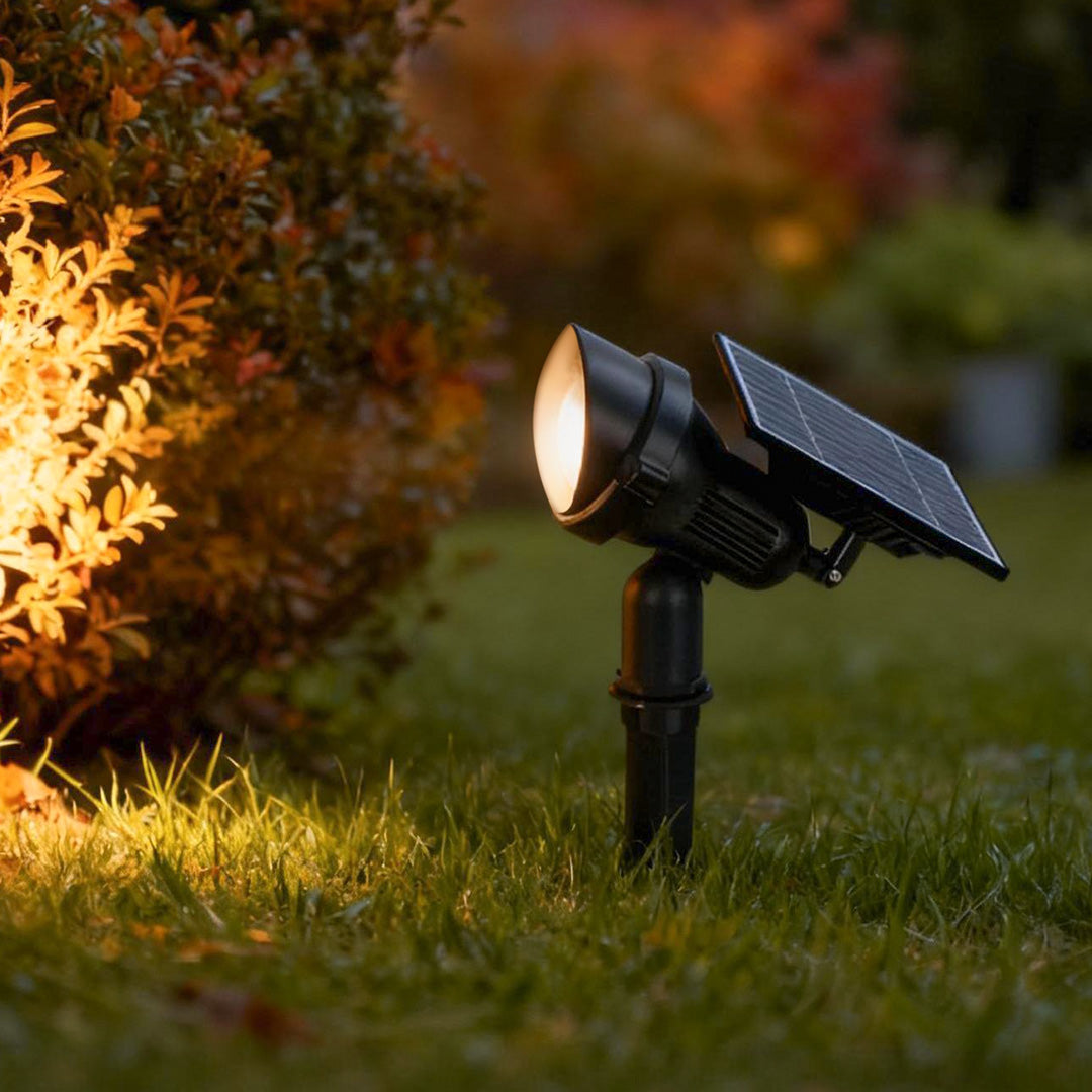 Lawn spot lights with solar panel and adjustable head, illuminating garden shrubs for warm outdoor ambiance
