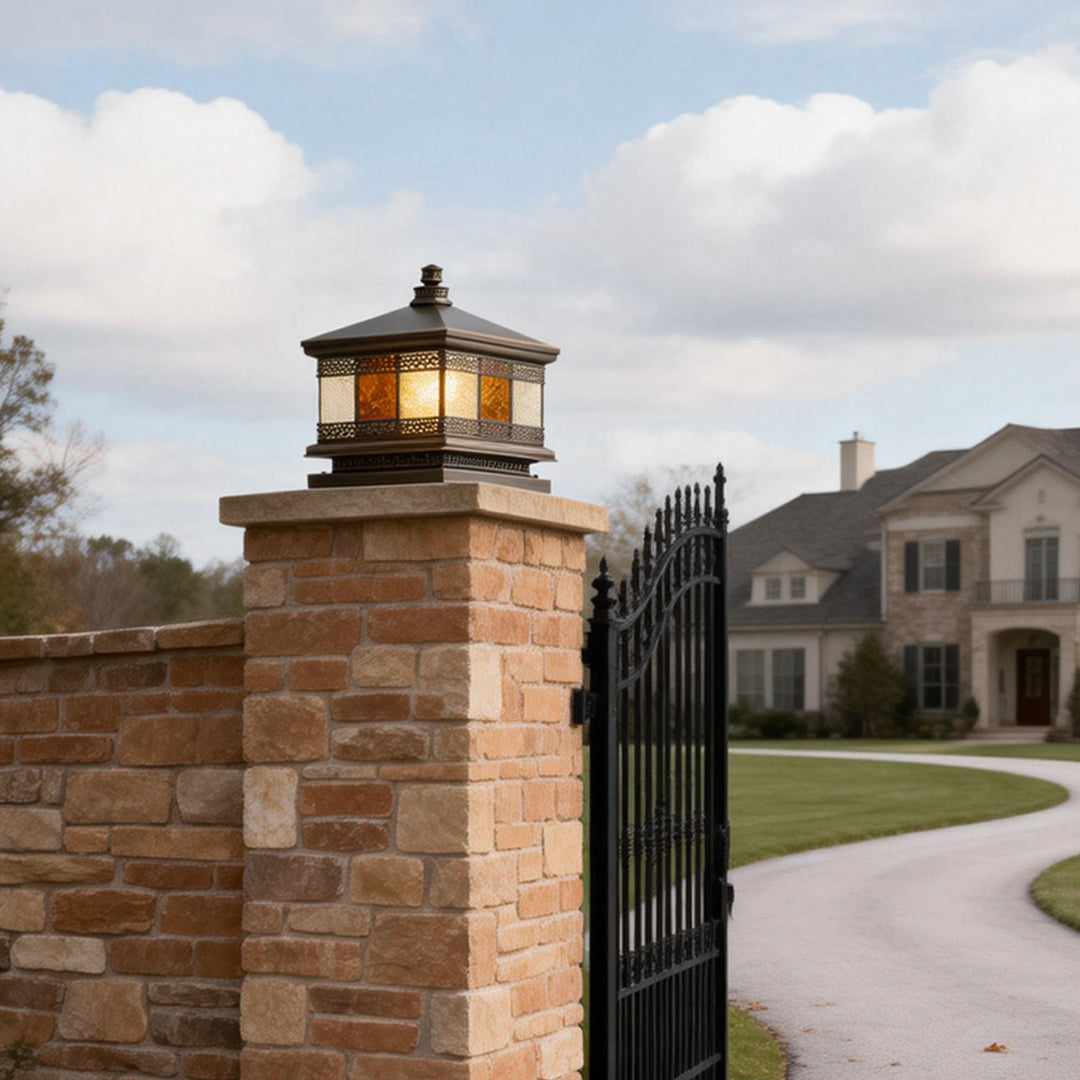 Solar column pillar lights installed on a brick gate pillar, casting a warm glow that highlights the entrance and surrounding landscape.