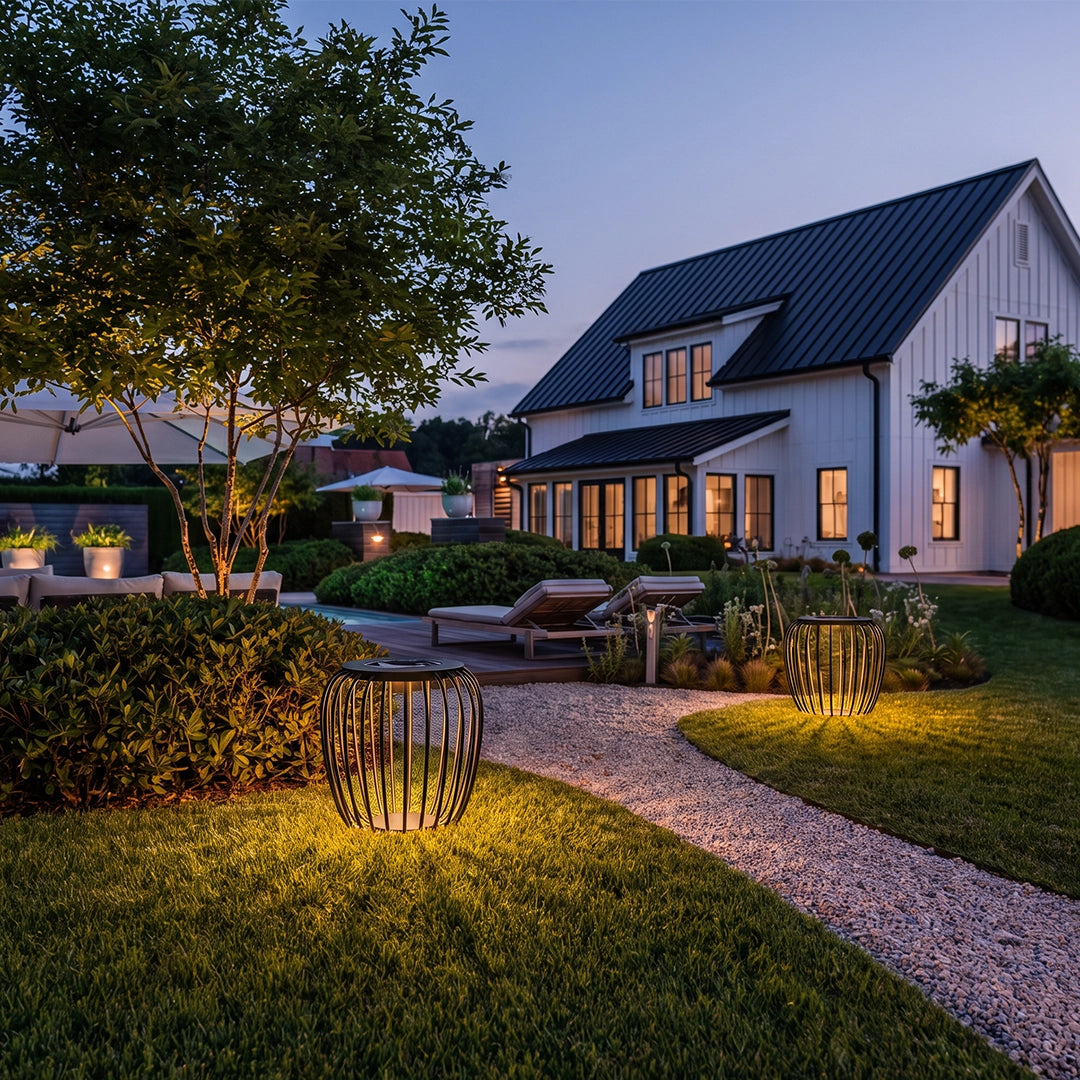 Solar garden lantern glowing beside a curved garden path in front of a modern house.