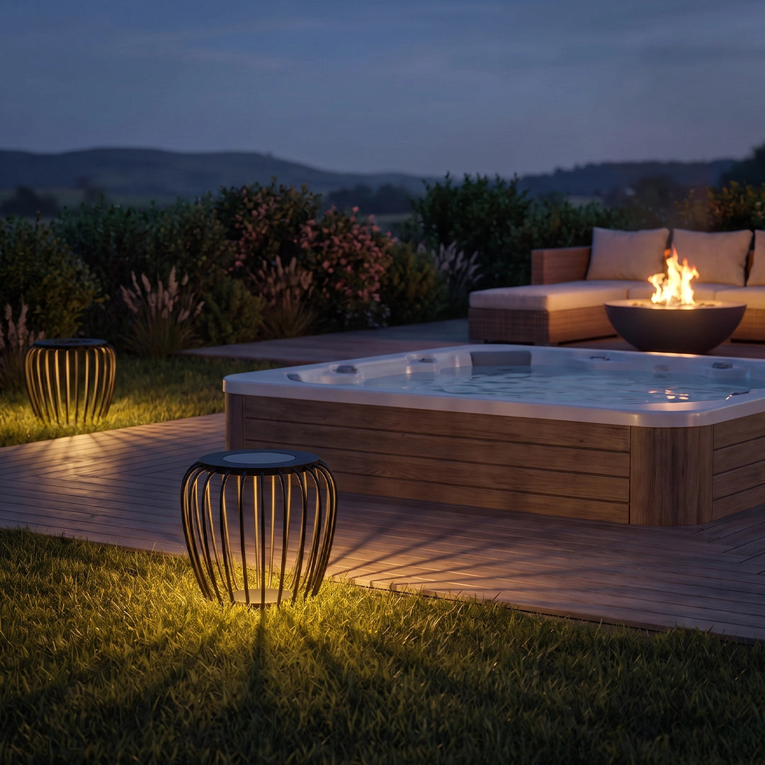 Solar garden lantern glowing beside a hot tub and deck in a landscaped backyard at night.