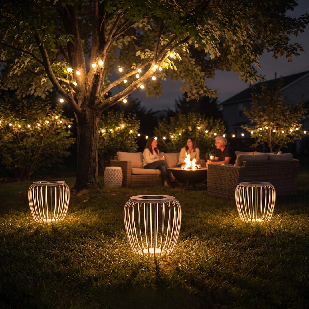 Solar garden lanterns glowing on a lawn beside outdoor seating and string lights at night.