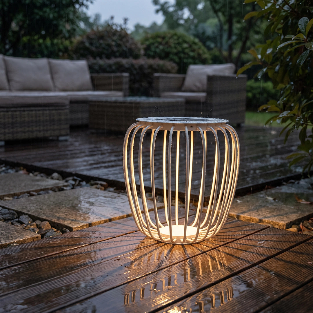 Solar garden lantern glowing on a wet patio beside outdoor seating and garden plants.