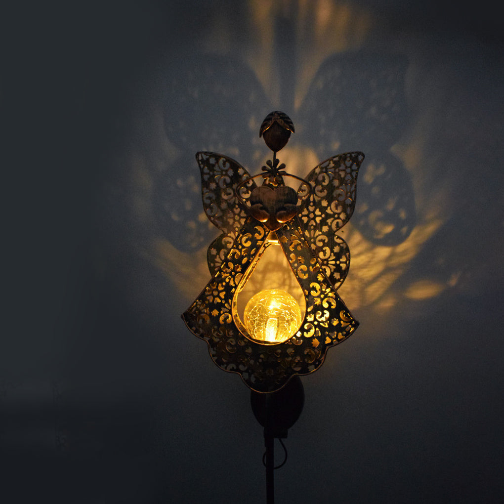 Angel-shaped solar garden stake light casting decorative shadows on an outdoor wall.