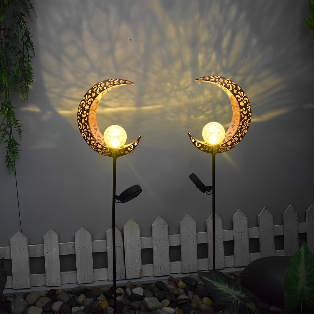 Solar garden stake lights with crescent moon shades glowing beside a white garden fence.