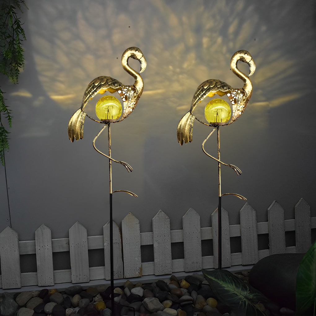 Flamingo solar garden stake lights creating patterned illumination beside a white garden fence.
