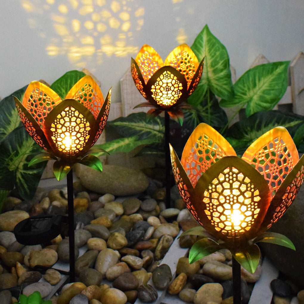 Lotus solar garden stake lights glowing among green plants and decorative garden stones.