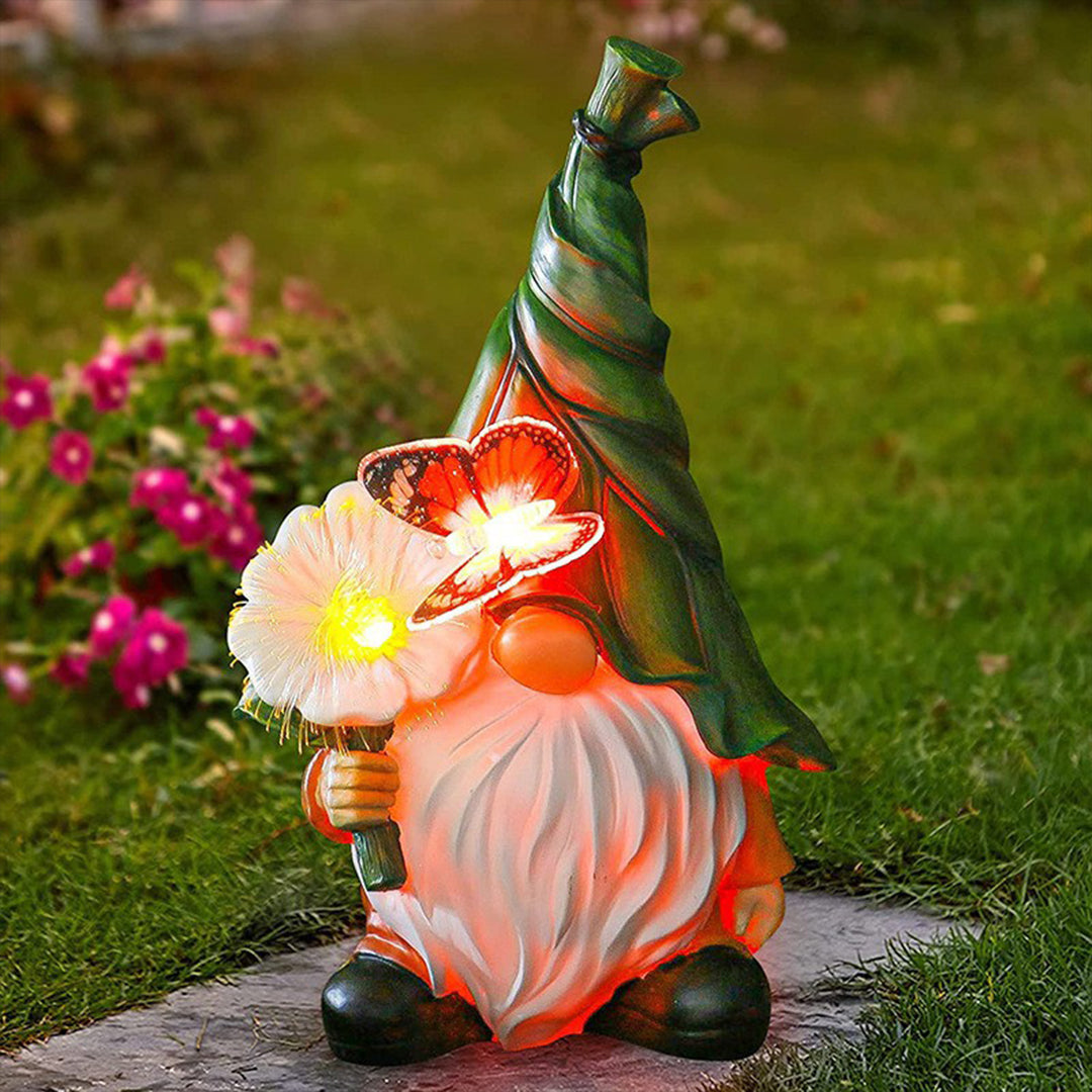 Solar-powered gnome with LED flower light glowing warmly in garden setting at dusk