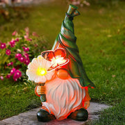 Solar-powered gnome with LED flower light glowing warmly in garden setting at dusk