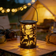 Solar hollow out lantern with deer and tree cut-out design, glowing warmly on an outdoor table.