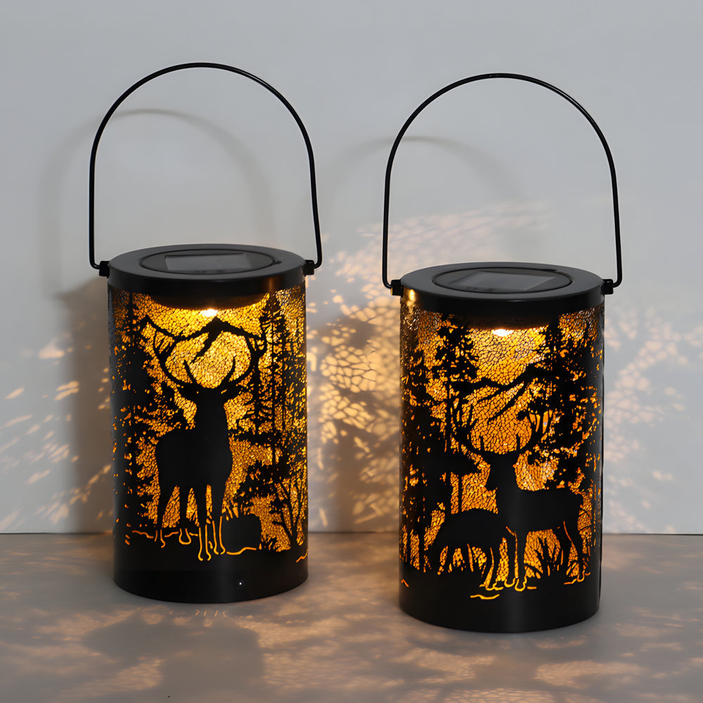 Two solar hollow out lanterns with deer and tree patterns, glowing on a garden table.