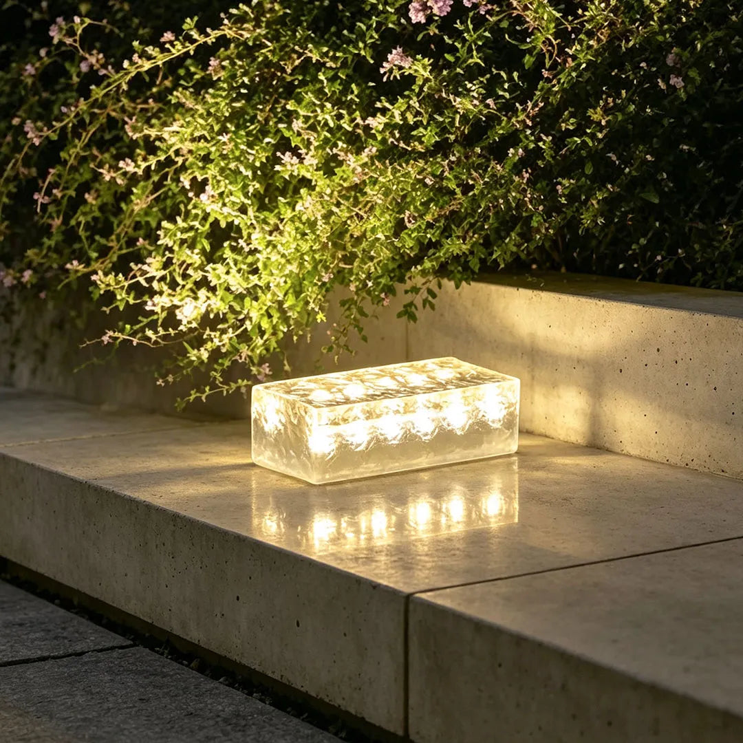 Solar LED step light glowing on a concrete ledge, illuminating nearby plants at night.