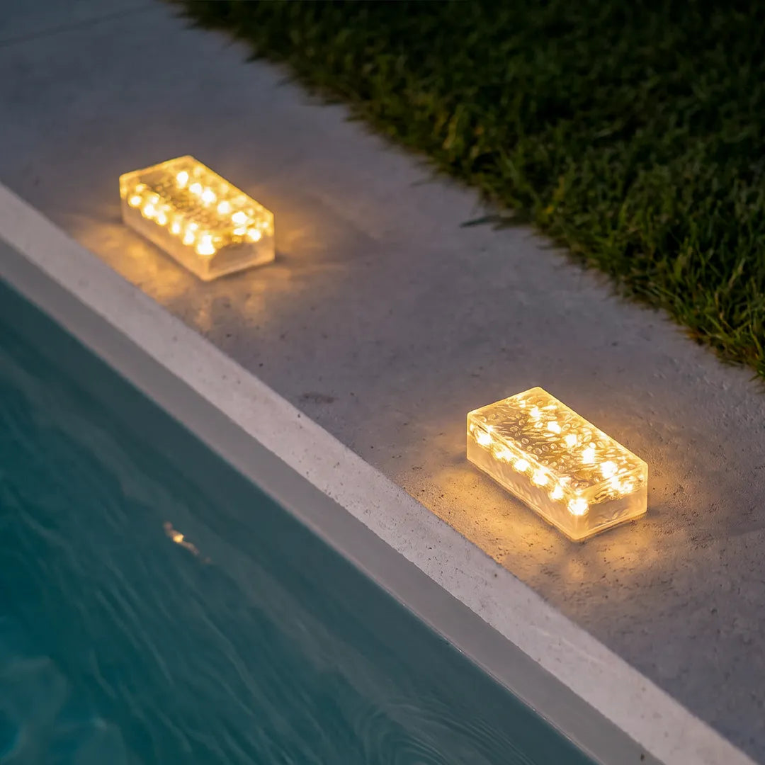 Solar LED step lights placed beside a pool edge, casting warm light on a concrete walkway.