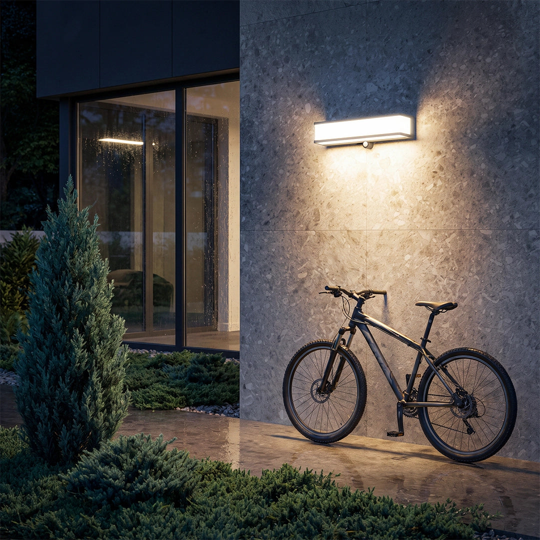 Solar light outdoor wall mount illuminating a concrete wall beside a bicycle and garden path.