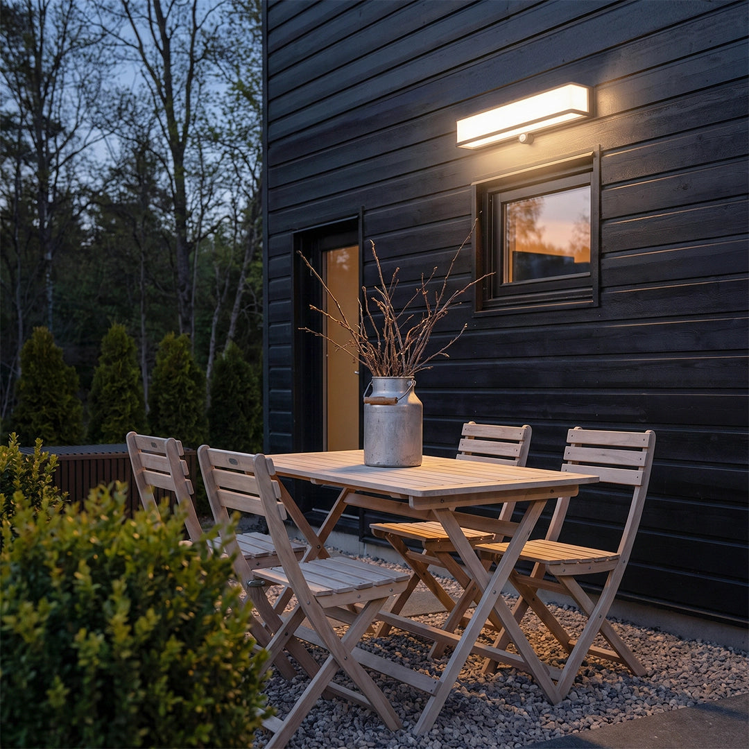 Solar light outdoor wall mount illuminating an outdoor dining area beside a dark exterior wall.