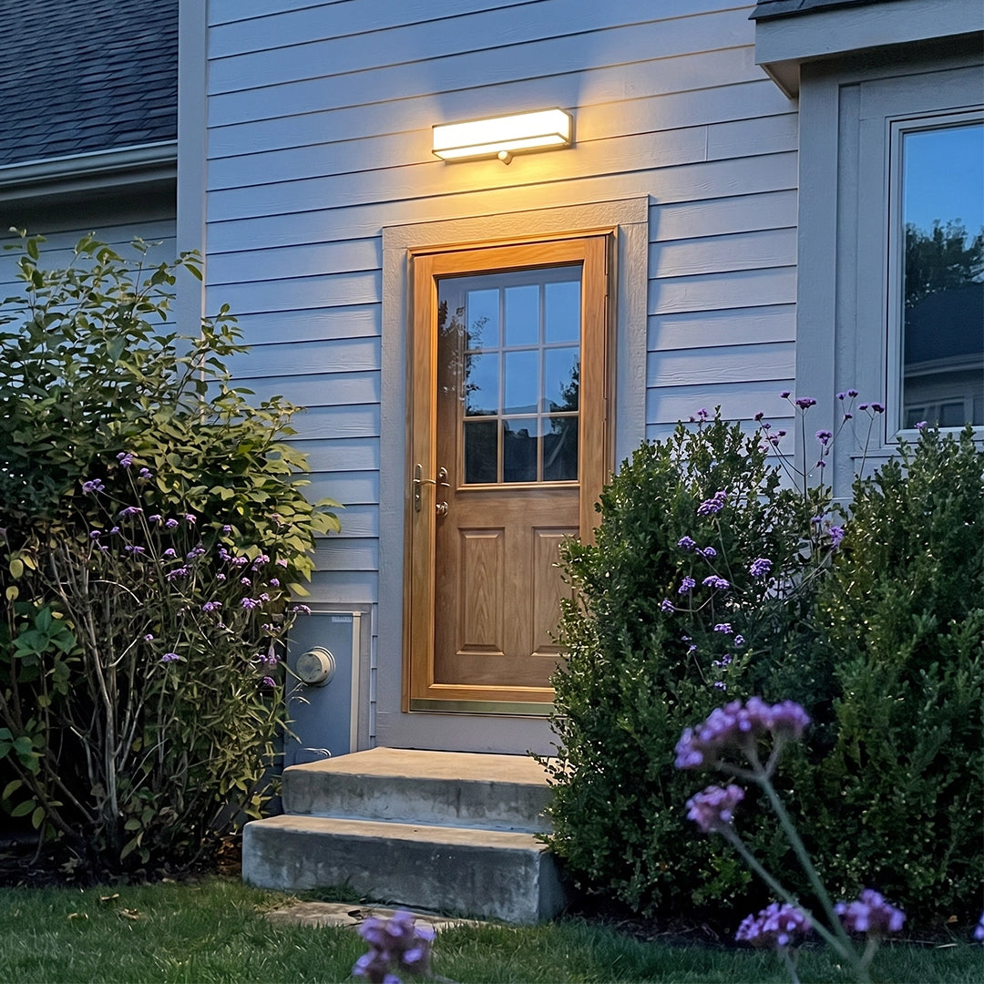 Solar light outdoor wall mount above a front door, lighting a small entryway and garden shrubs.