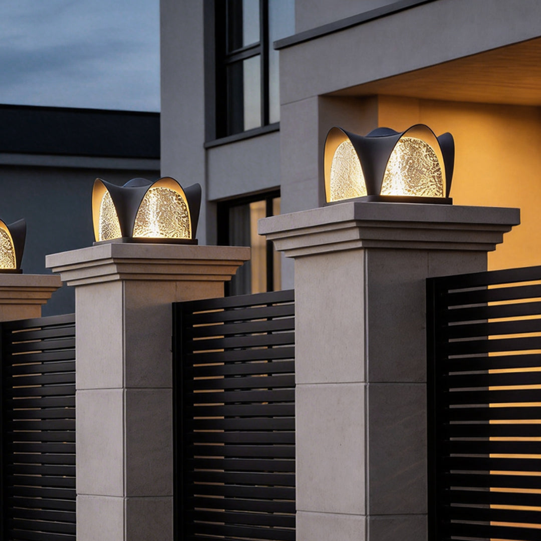 Solar light pillar with a sleek black finish, providing warm light near a fence.
