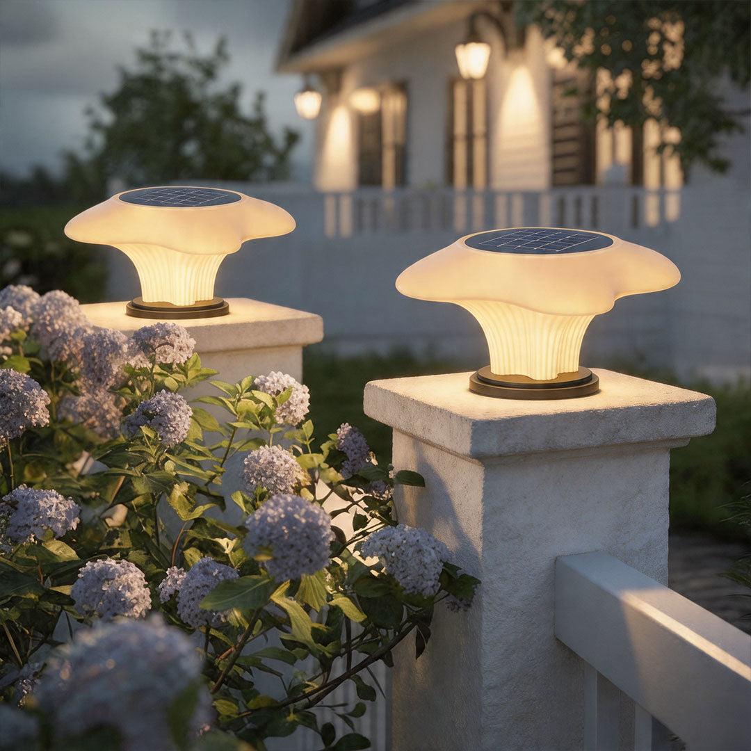 Solar pillar light mounted on garden wall pillars beside blooming flowers with warm evening glow.
