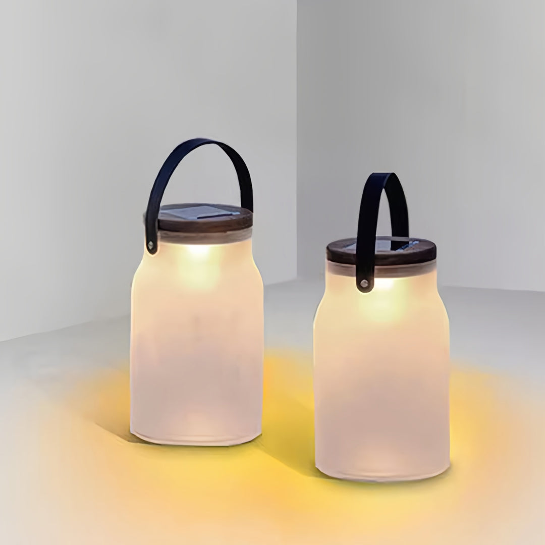 Pair of modern solar powered camp lanterns on a table, emitting soft warm light in a clean minimal setting.