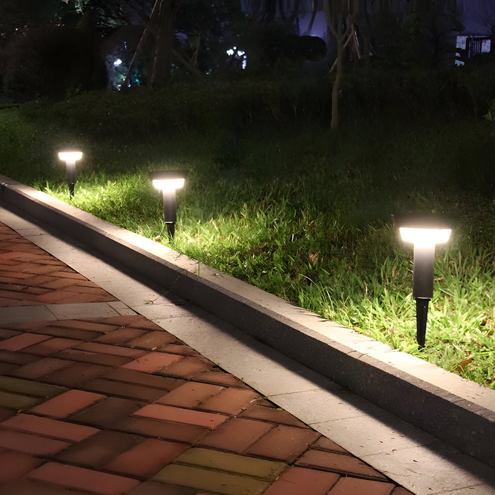 Solar powered garden path lights illuminating a brick pathway edge in a residential outdoor landscape at night.