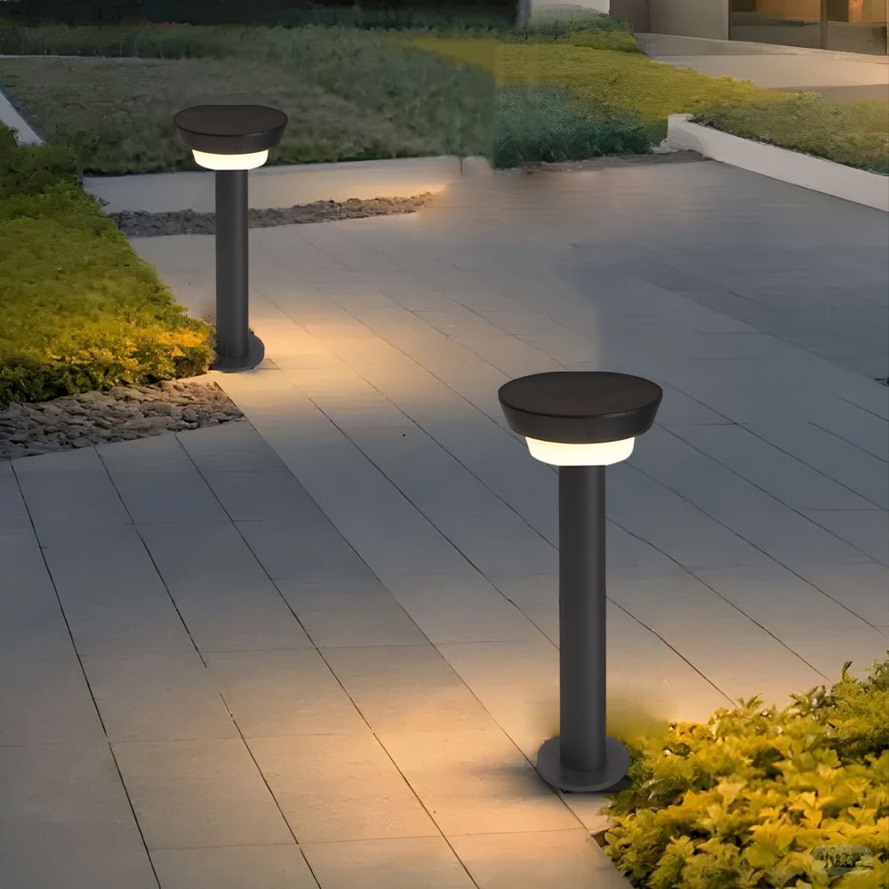 Solar powered garden path lights lighting a paved patio walkway surrounded by low plants and greenery.